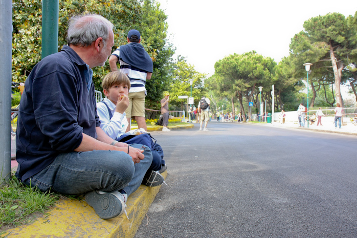 2人で観戦に来た祖父と孫が沿道に腰掛けて選手の通過を待つ