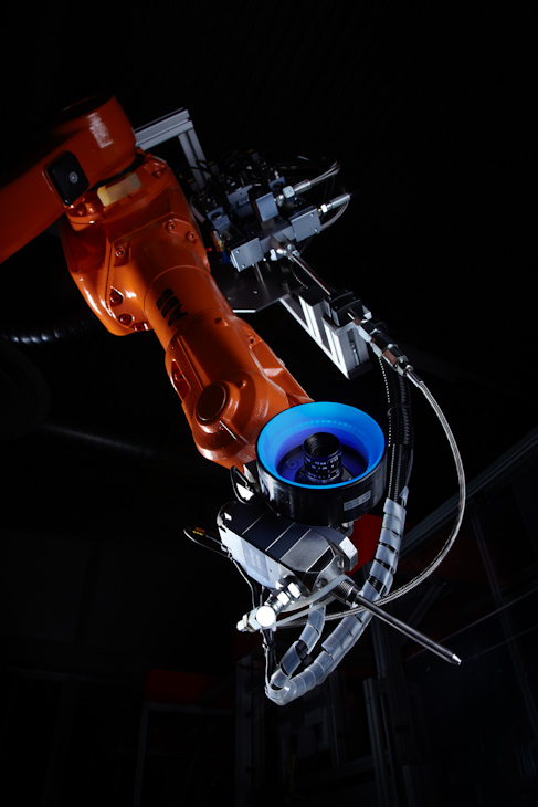 ラグの接着を行なうロボット　ブルーのライトがラグを照らし、カメラで接着剤の量を確認する