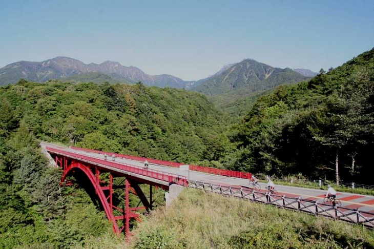 八ヶ岳連峰をバックに、川俣川渓谷に掛る東沢大橋を走行。通称「赤い橋」と呼ばれる絶景ポイント