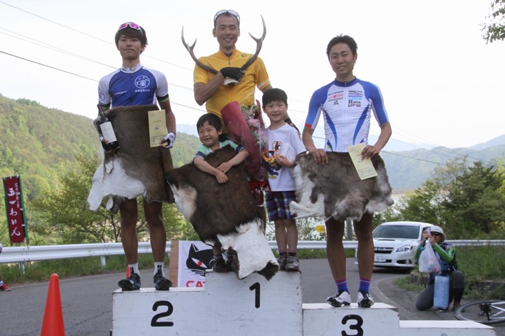 子供たちと一緒に表彰台に上る総合優勝の高岡亮寛（イナーメ）、2位に間瀬勇毅（京都産業大学）、3位に風間博之（サイクルフリーダム）