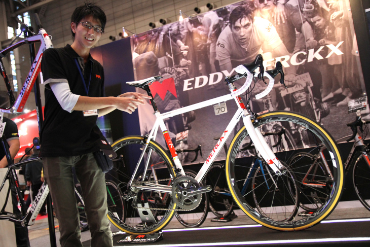 ブース正面に飾られたエディ・メルクス生誕70周年モデルEDDY70と、ブースを案内してくれた深谷産業の赤田匠さん