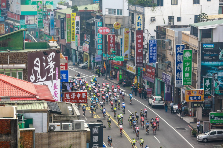 突き出し看板が立ち並ぶ台湾らしい市街地を走るプロトン