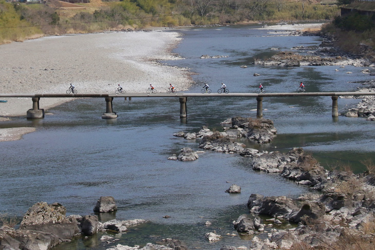 四万十川の沈下橋を渡るPR隊一行。サイクリストなら誰もが走ってみたいと夢見る光景だろう