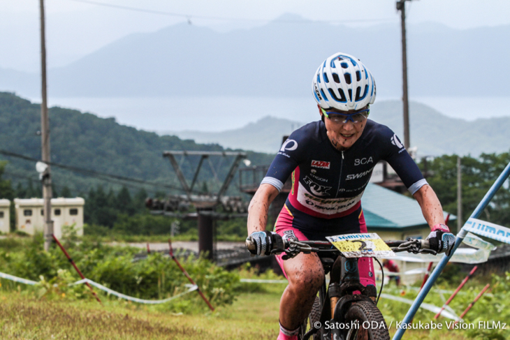 田沢湖を背中にゲレンデを登る小林可奈子(MTBクラブ安曇野)