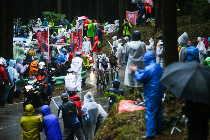 雨具に身を包んだ観客を縫って進むトマ・ルバ（フランス、キナンサイクリング）ら