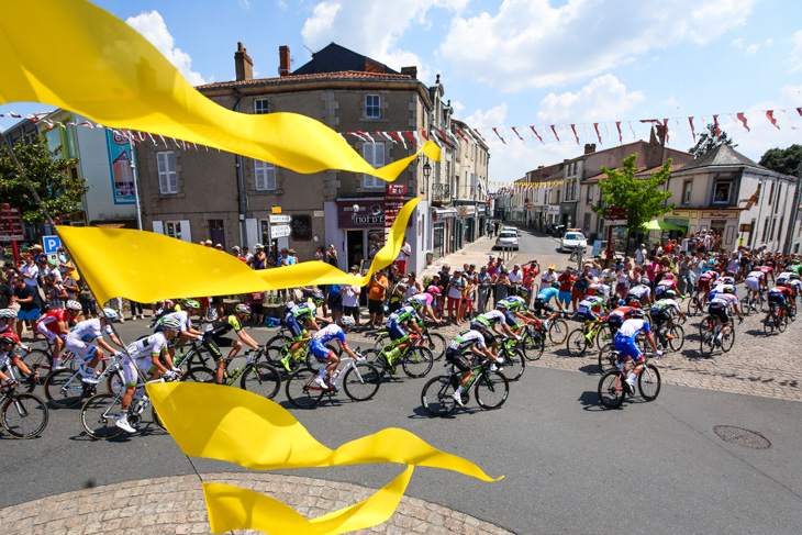黄色に彩られた町を通過していくツール・ド・フランスのプロトン