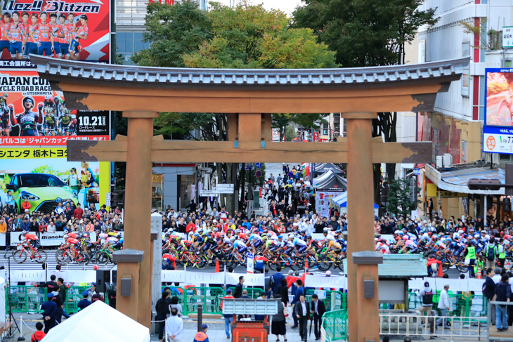 宇都宮大通りの二荒山神社の鳥居を横目に駆け抜けるプロトン