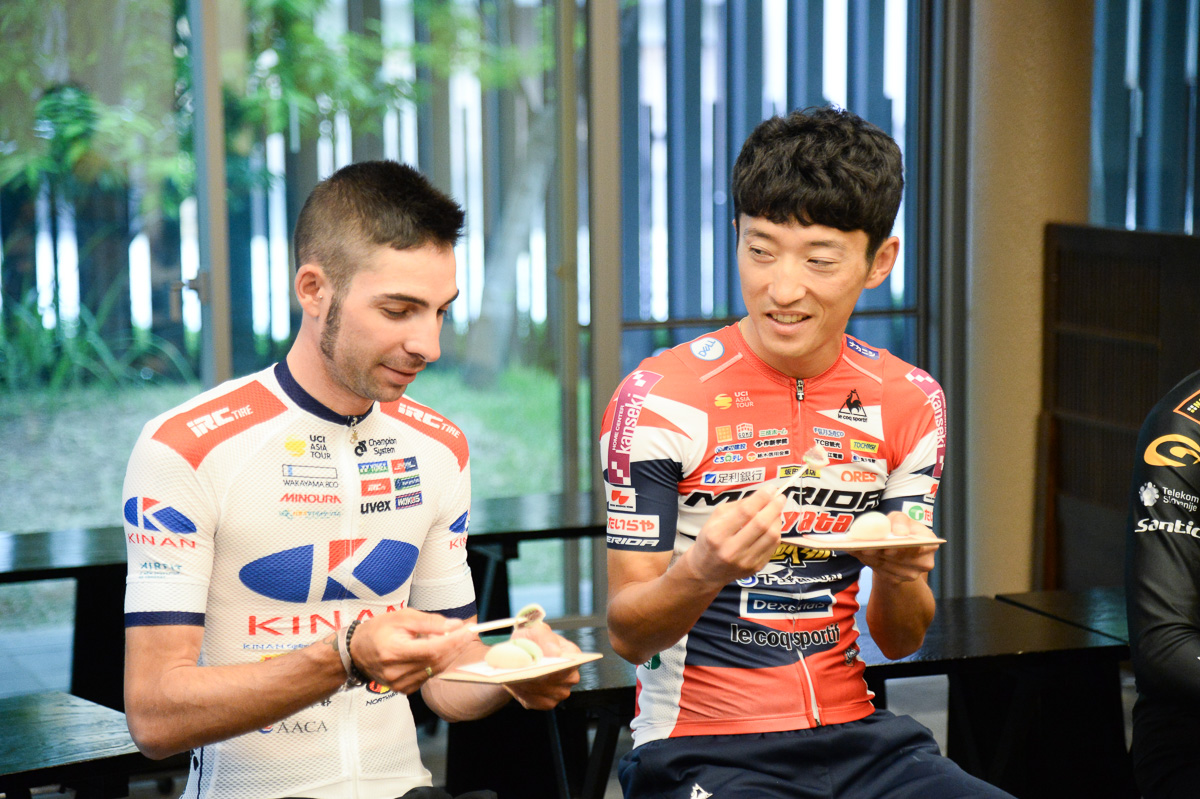 見よう見まねでお菓子を食べるマルコス・ガルシア(キナンサイクリングチーム)と増田成幸(宇都宮ブリッツェン)