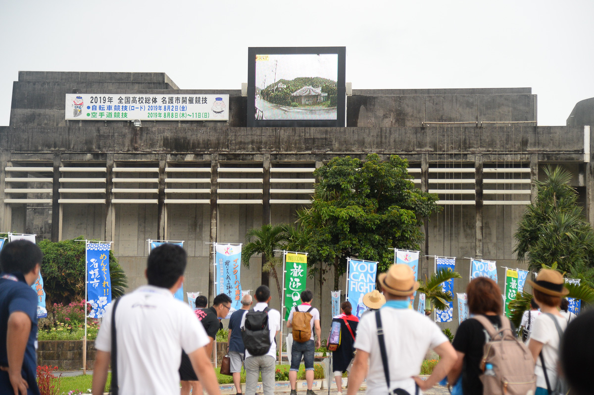 名護市中央会館に設置された大型モニターでコース途中の映像に見入る観客