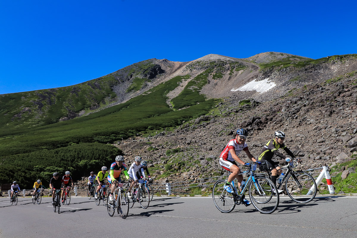 盛夏で白の面積を減らした大雪渓前を行くサイクリストたち