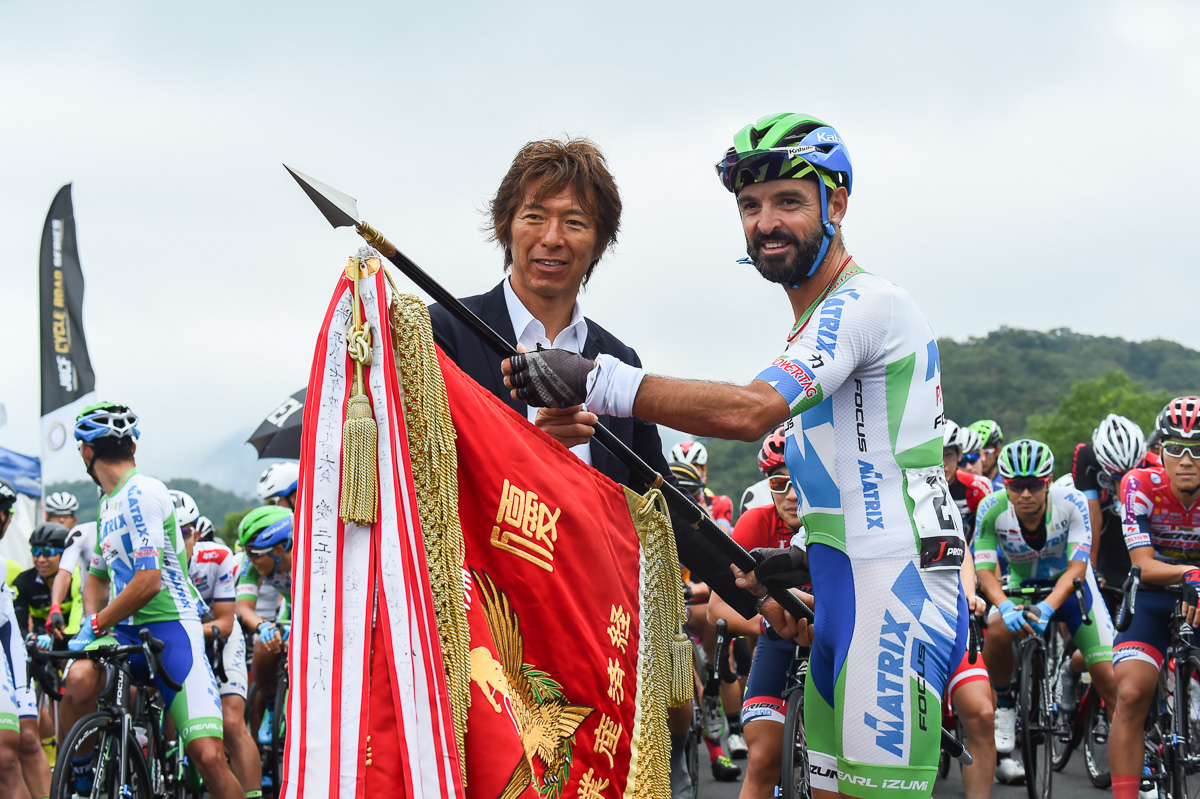 昨年優勝のフランシスコ・マンセボ(マトリックスパワータグ)から、輪翔旗が今中大介JBCF副理事長に返還される
