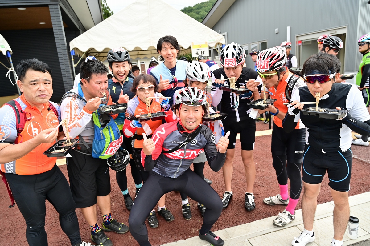 ゲストライダーの土井ちゃんの後ろで麺をすする参加者たち