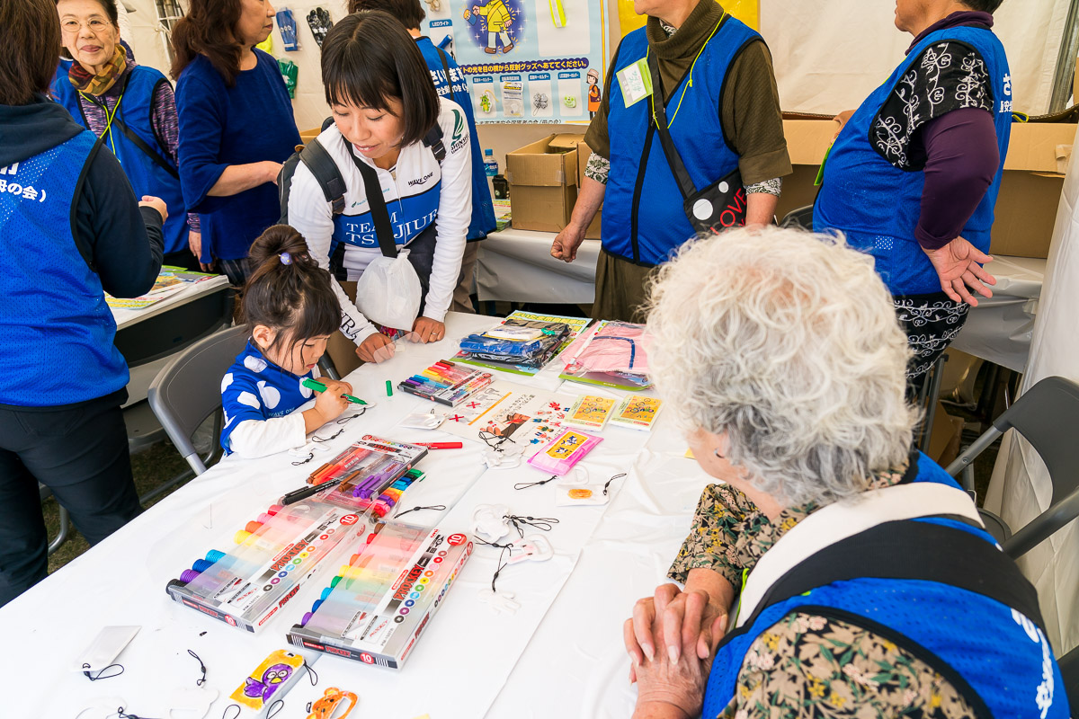 母の会のベテランお母さんが、反射材付き交通安全お守りをペイントする子どもを見守る