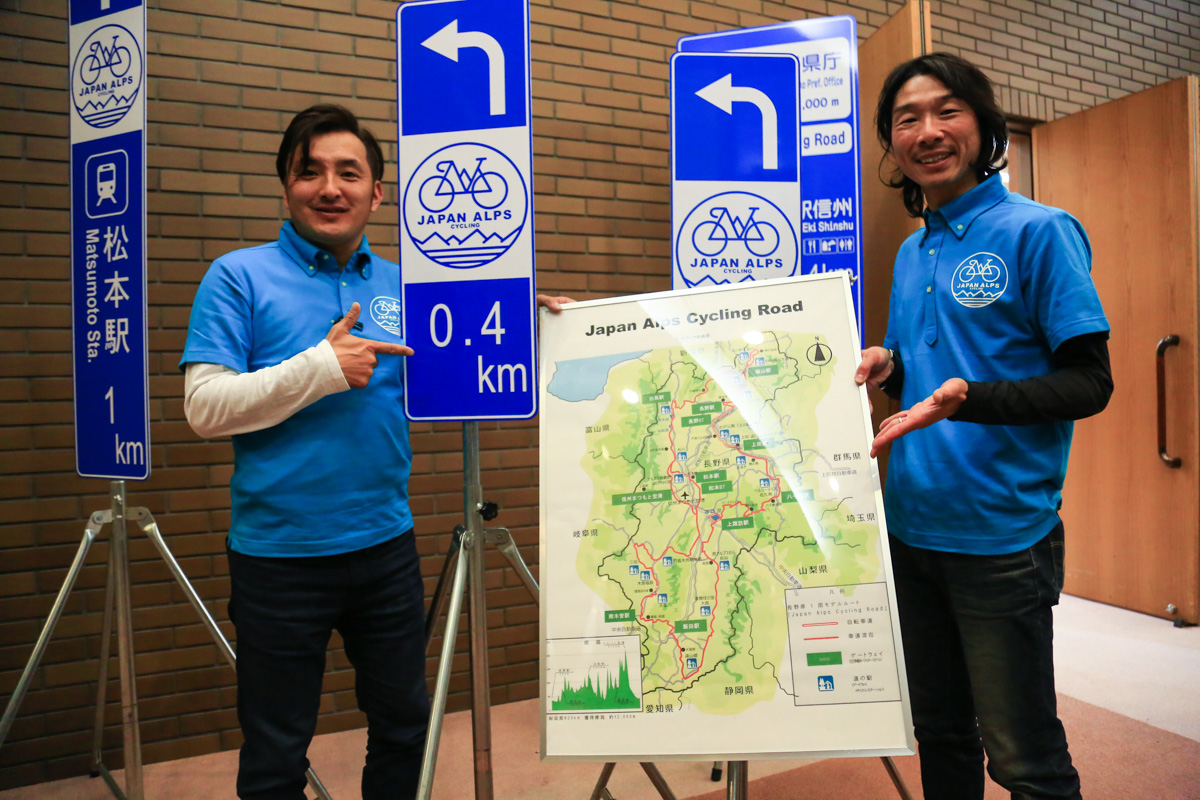 Japan Alps Cyclingプロジェクト 「ジャパンアルプスサイクリングロード」マップや道路標識を前に
