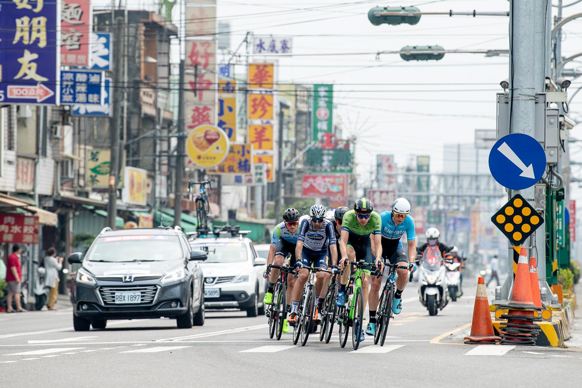 漢字が賑やかな看板の街並みを背に5人の逃げ集団が行く