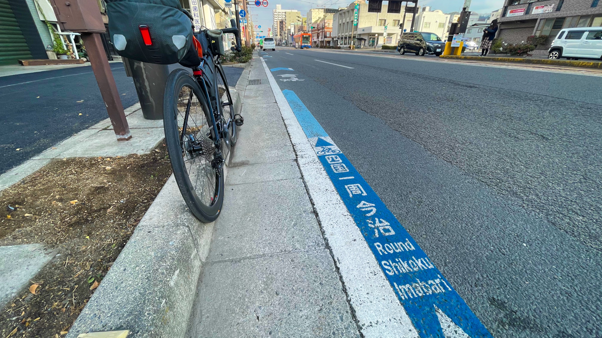 松山市街にさっそく四国一周サイクリングのルートを示すブルーラインと路面ピクトが現れる