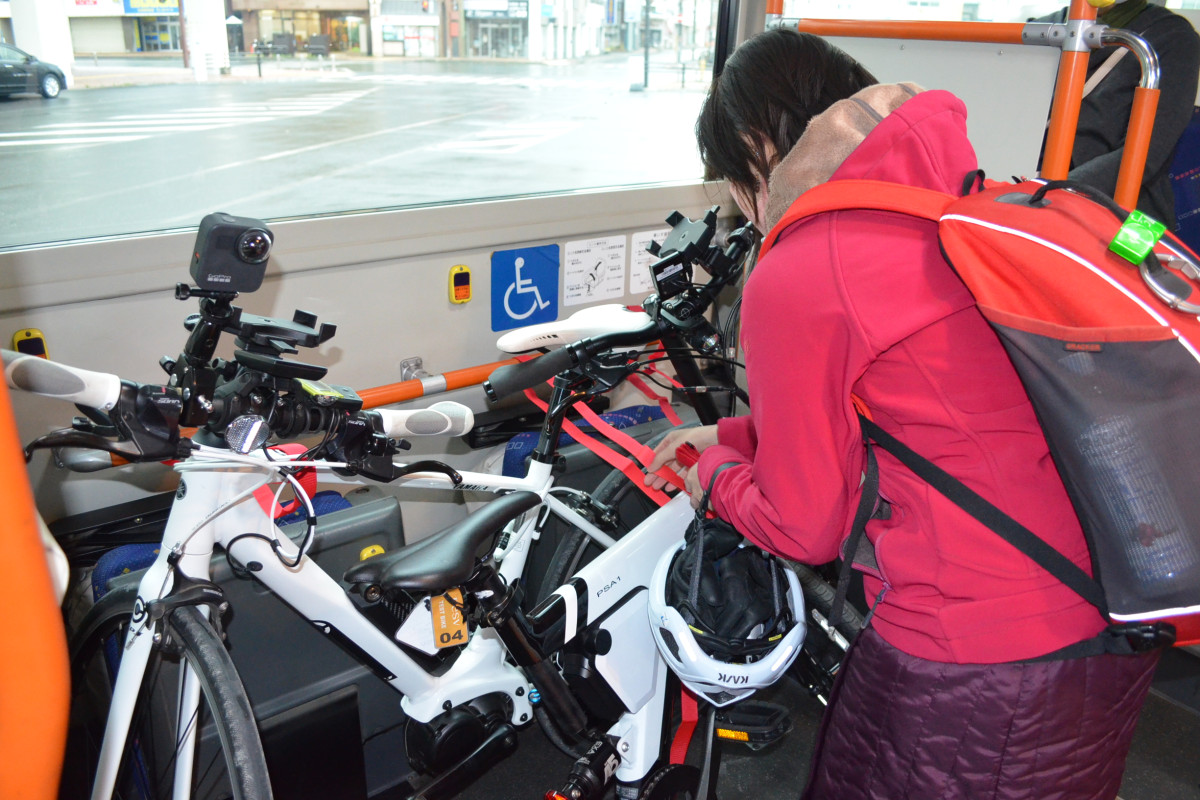 バスの車椅子エリアに自転車を載せ、指定のベルトで固定する＞