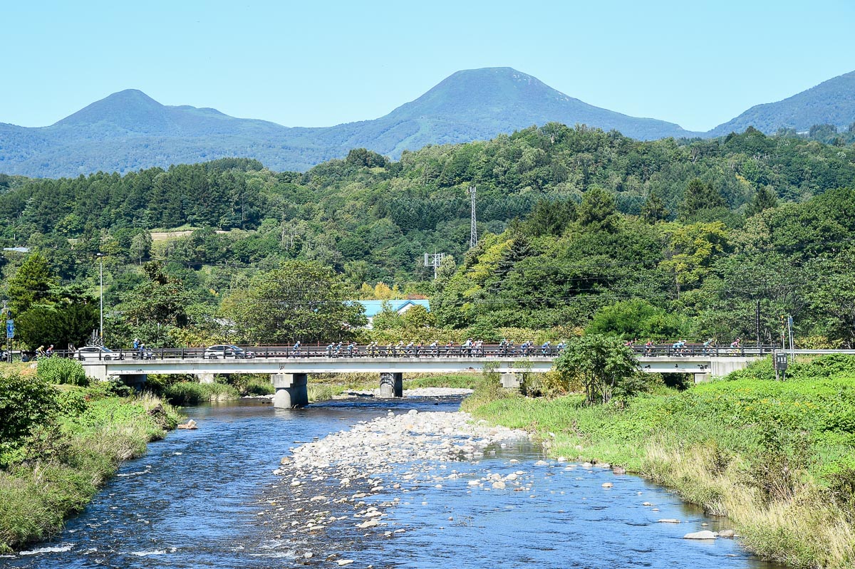110km地点付近 昆布川を渡るメイン集団 奥に見えるのはニセコ連峰