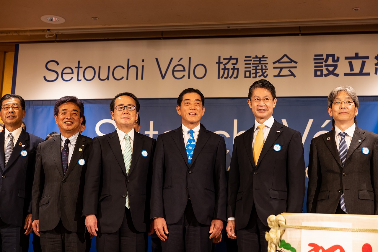 鮮やかなブルーに自転車がデザインされたネクタイを締める中村愛媛県知事。左は次回総会開催県の池田豊人香川県知事