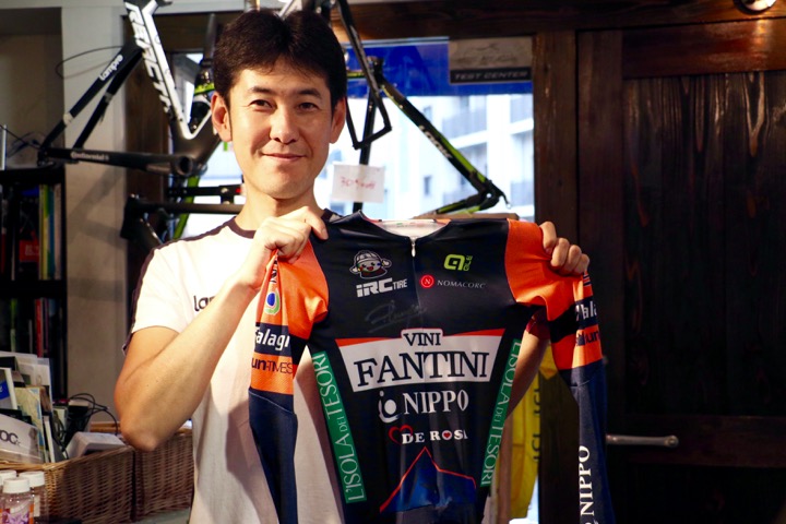 熱烈な海外ロードレースマニアでもある店長の杉山友則さん。手にしているのはダミアーノ・クネゴのサイン入りワンピース